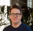 Smiling man with black glasses and a dark blue shirt.
